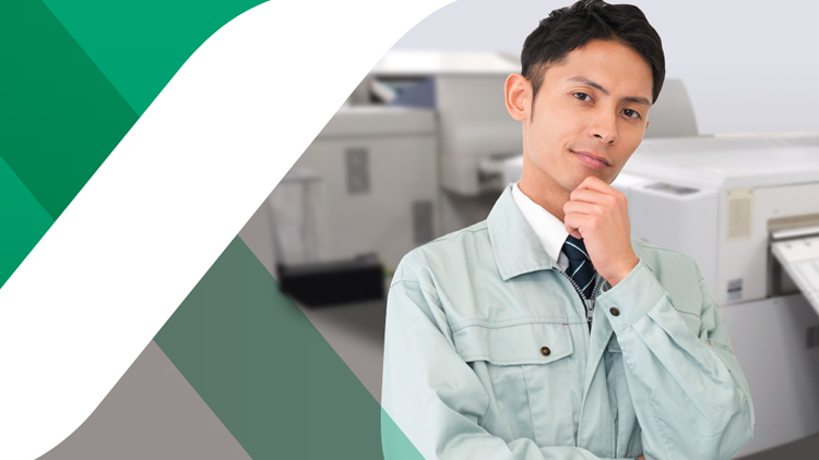 印刷機の前でポーズをとる作業着を着た男性