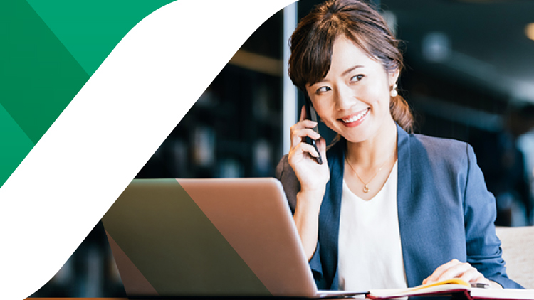 パソコンの前で笑顔で電話するフォーマルな格好をした女性