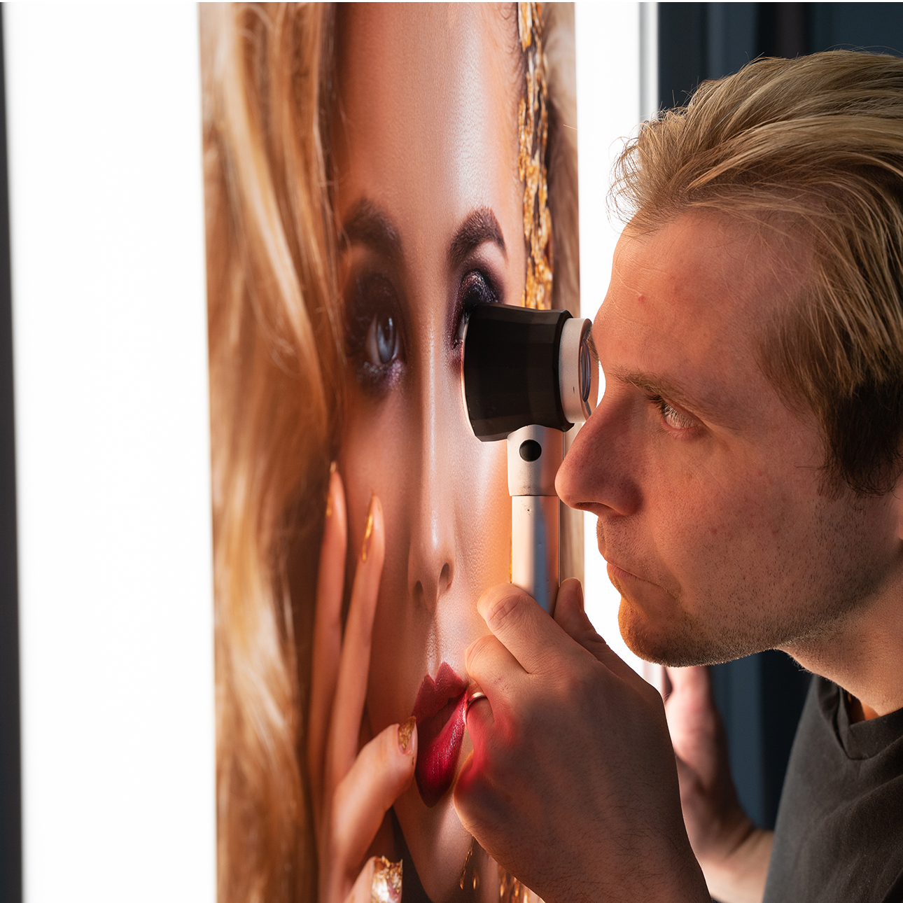 A person examining a close-up portrait of a woman using a handheld magnifying device.