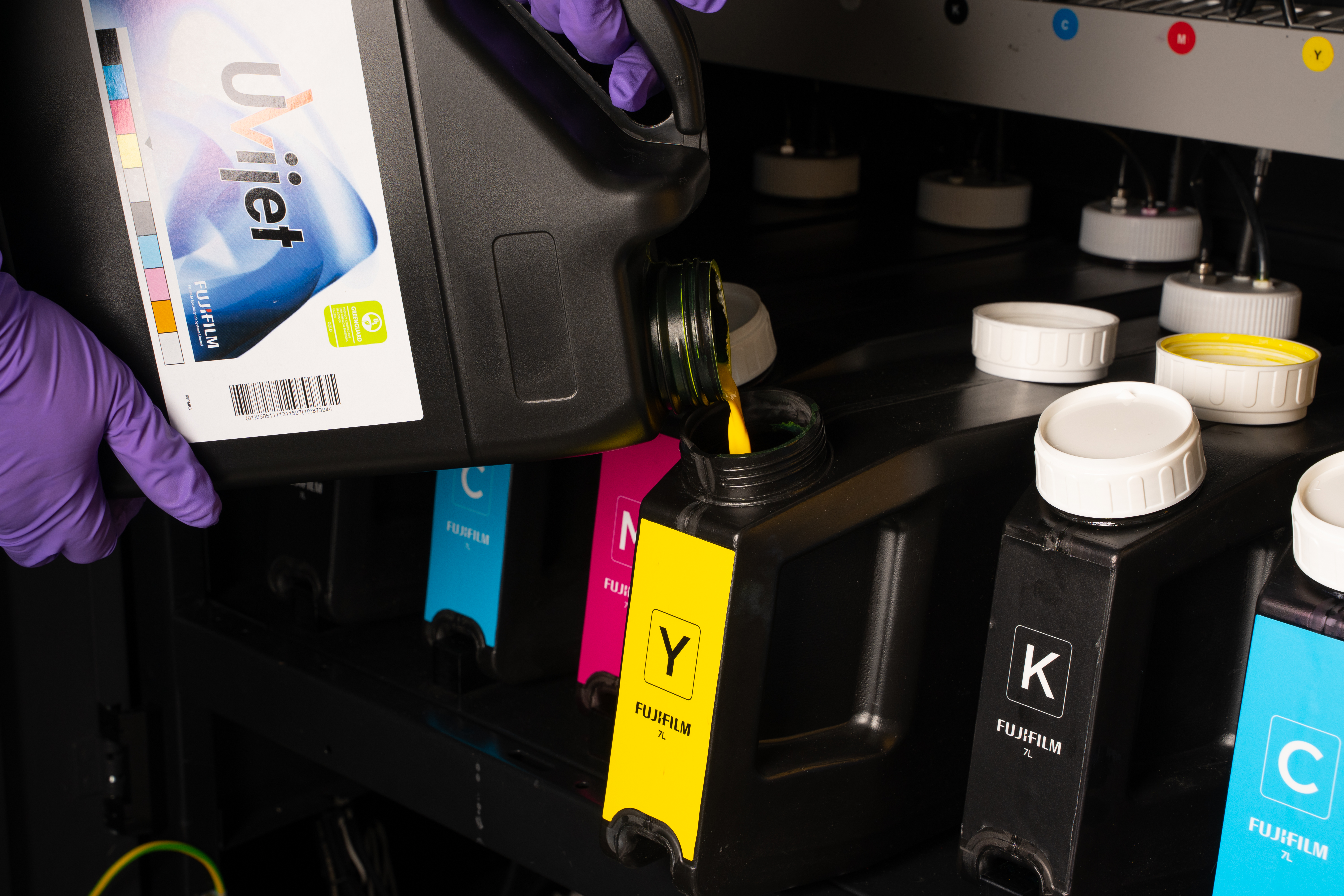 Gloved hands pouring yellow ink from a container into a large yellow ink tank.