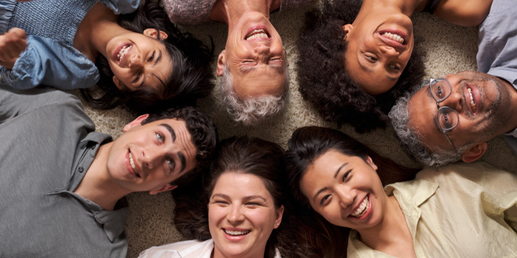 A diverse group of people gathering with smiles, lying down and looking up.