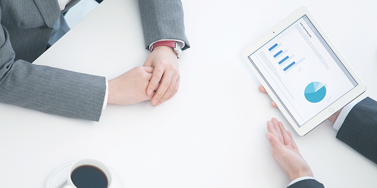 兩個人坐在白色桌子旁，其中一個人在講解平板電腦上的資料。