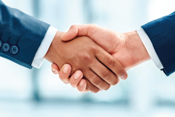 Two hands engaged in a handshake, symbolising agreement and partnership. One hand is dressed in a dark suit, while the other is in a light-coloured shirt. The background is blurred, emphasizing the handshake as the focal point of the image.