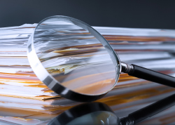 A magnifying glass placed over a stack of papers, with some sheets appearing slightly blurred and highlighted under the lens.