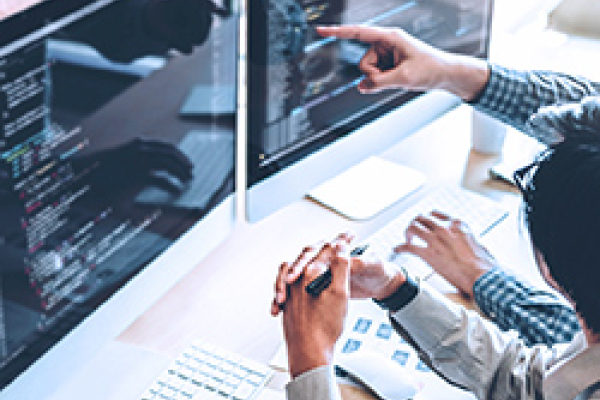 ภาพที่แสดงถึงสภาพแวดล้อมการทํางานร่วมกัน โดยมีบุคคลสองคนหารือกันอยู่ตรงหน้าจอคอมพิวเตอร์ บุคคลหนึ่งกําลังชี้ไปที่หน้าจอซึ่งแสดงผลบรรทัดโค้ด ในขณะที่อีกคนหนึ่งใจจดใจจ่อไปกับแป้นพิมพ์ ฉากนี้แสดงให้เห็นถึงสภาพแวดล้อมการทํางานเป็นทีมในสาขาที่เกี่ยวข้องกับเทคโนโลยี โดยเน้นไปที่การเขียนโค้ดหรือการพัฒนาซอฟต์แวร์ พื้นที่ทํางานมีความทันสมัยและมีแสงสว่างเพียงพอ ซึ่งเอื้อต่อบรรยากาศการทํางานที่มีประสิทธิภาพ